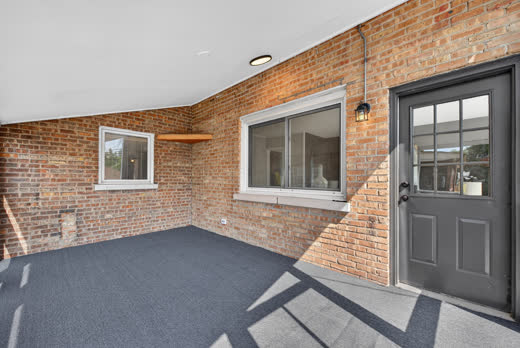 Carpeted screened porch with exposed brick and gray entry door at 9205 S Utica Ave